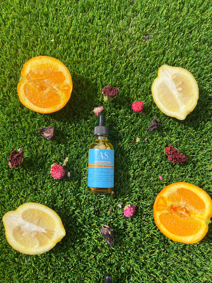 Amor Sui Multi-Purpose Botanical Oil surrounded by fresh citrus slices and flower petals on green grass.