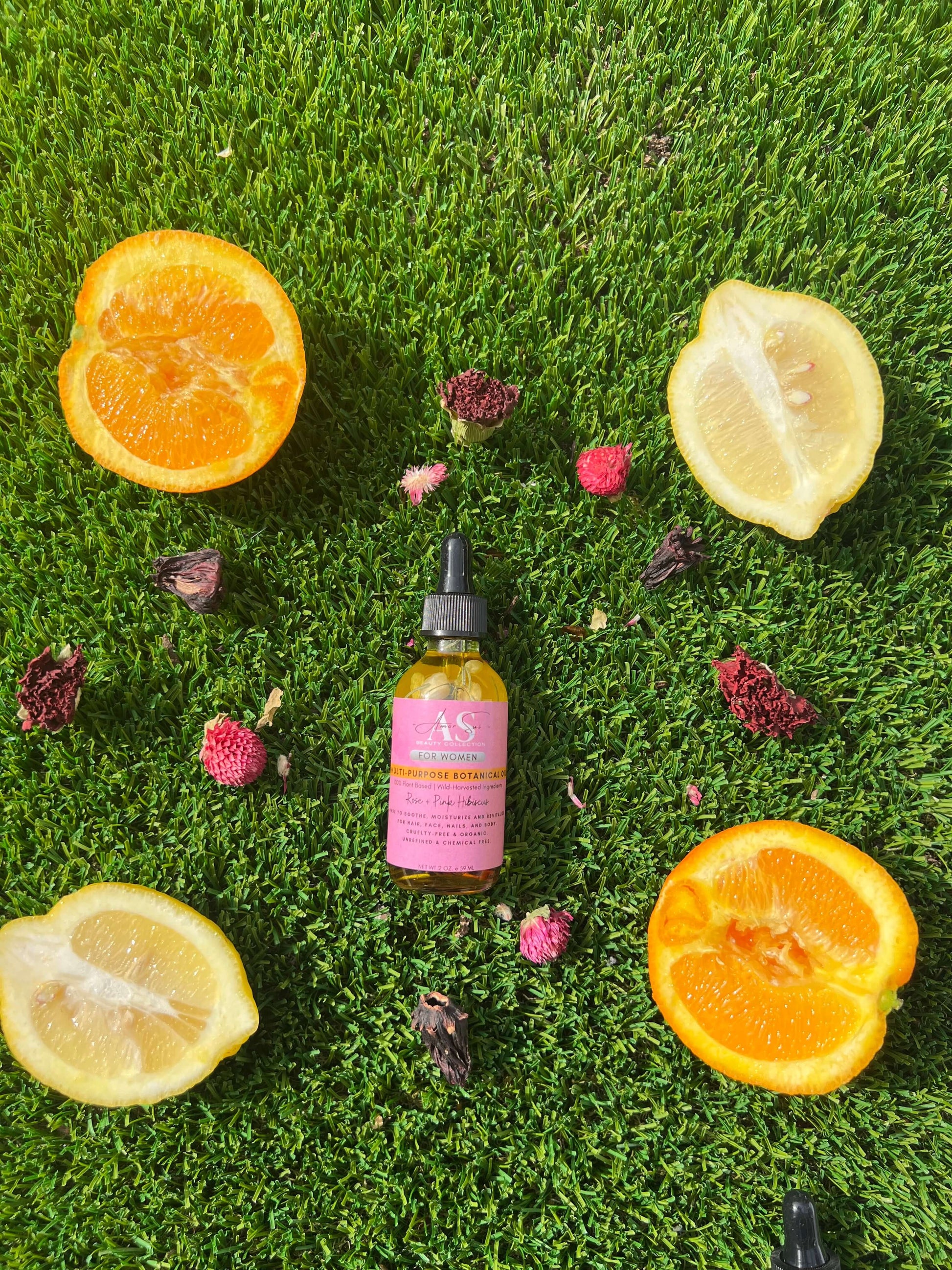 Amor Sui Multi-Purpose Botanical Oil bottle surrounded by fresh orange and lemon halves on green grass.