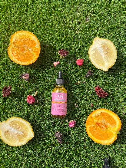 Amor Sui Multi-Purpose Botanical Oil bottle surrounded by fresh orange and lemon halves on green grass.